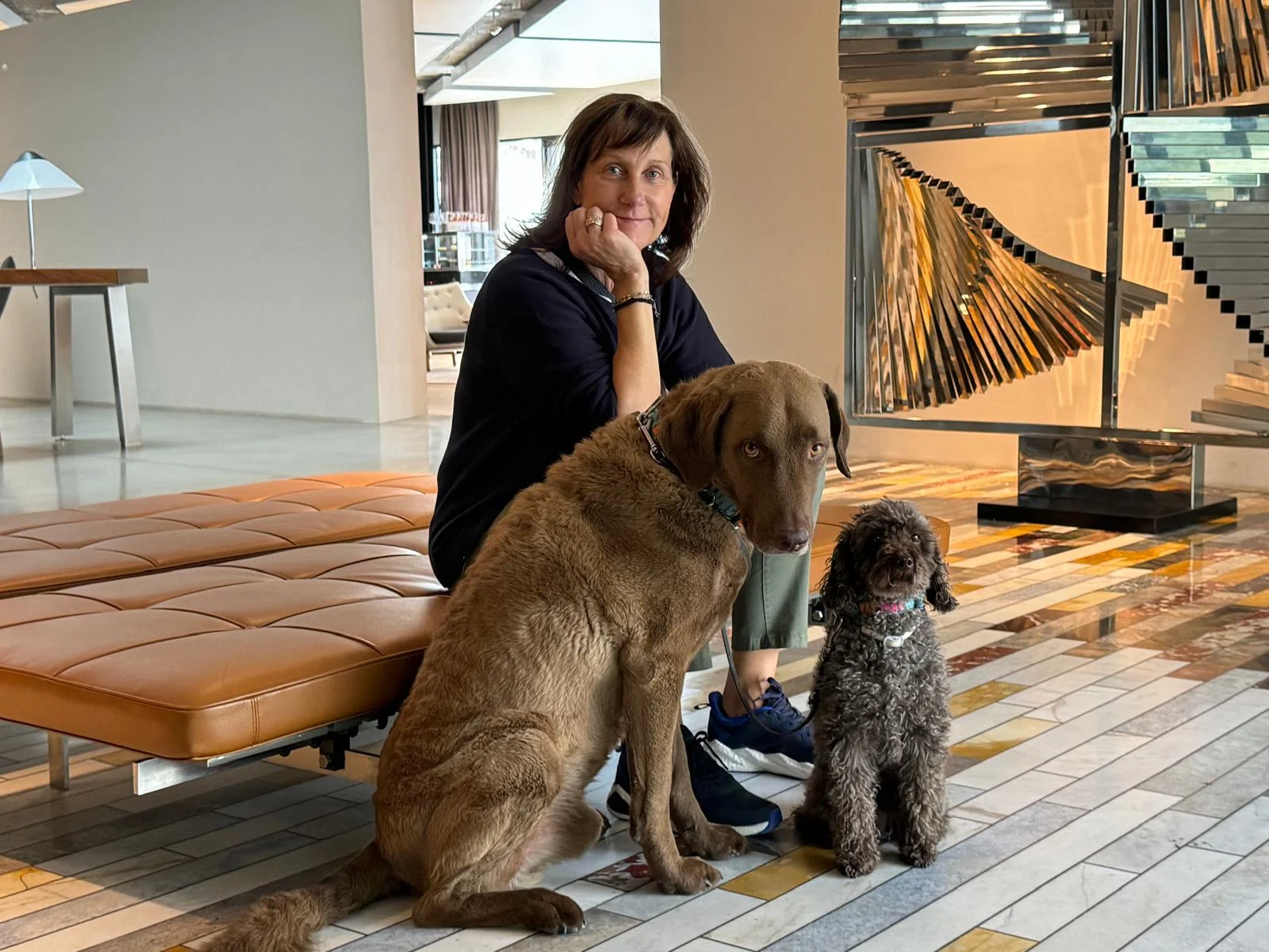 Petra sitzt mit ihren beiden Hunden in einem hellen Innenraum